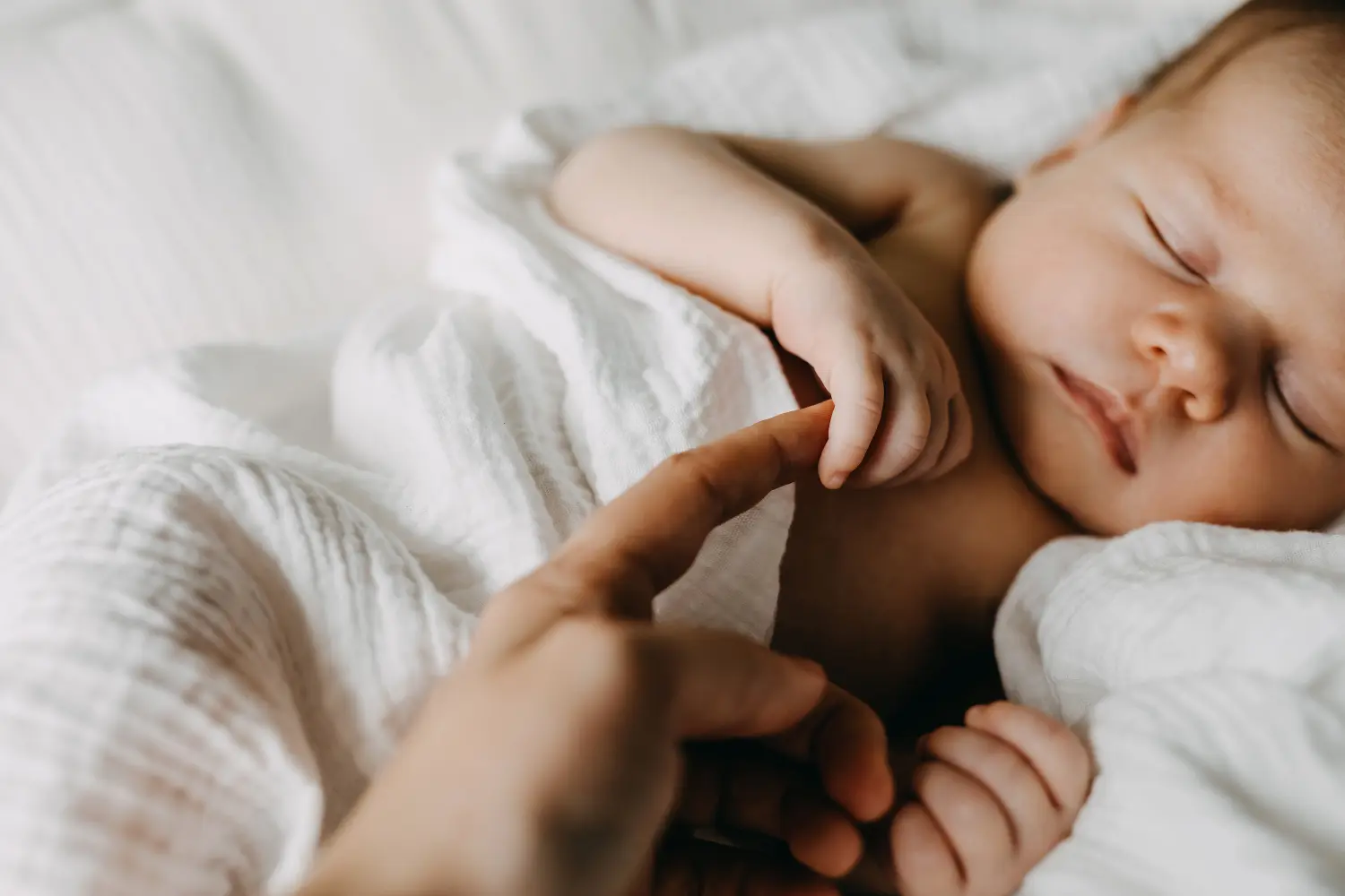 Nahaufnahme eines neugeborenen Babys, das den Finger der Mutter hält.