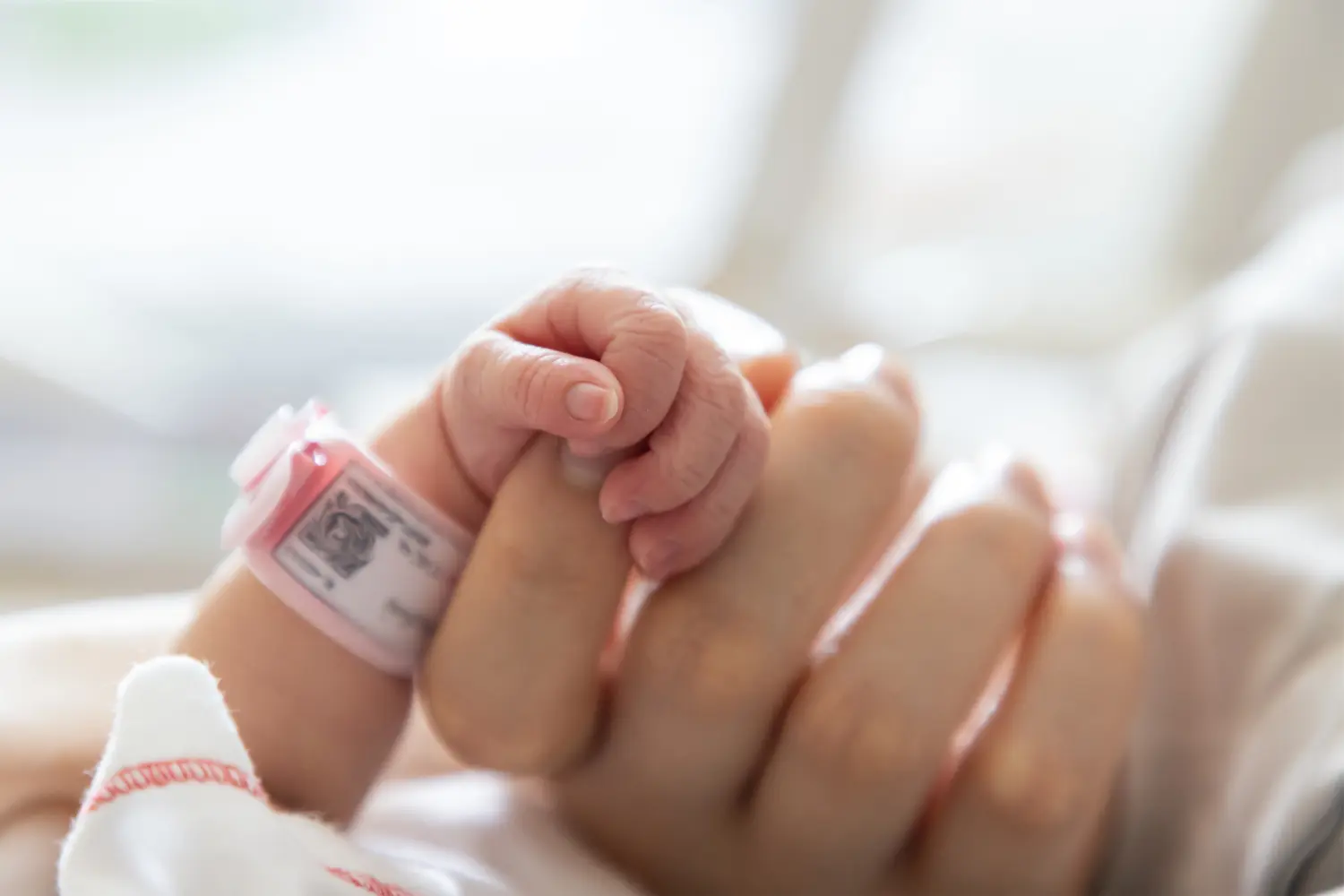 Neugeborenes Baby hält Mamas Zeigefinger in der Hand.